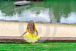 Little girl in yellow dress with long hair sit in summer Park on banks of river