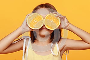 A little girl in a yellow dress, on an orange background, balks, closes her eyes with oranges.