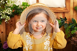 Little girl in a yellow dress smiles and holds a straw hat. Childhood concept. Portrait of cute little blond girl in countryside,