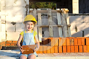 Little girl in a yellow hardhat is playing builder on the construction site of her future home. Expectation of moving, choosing a