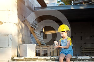 Little girl in a yellow hardhat is playing builder on the construction site of her future home. Expectation of moving, choosing a