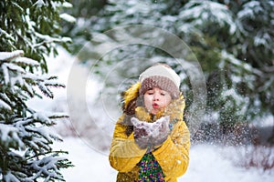 A little girl in a yellow jacket plays with snow in the winter. The child holds the snow in his hands