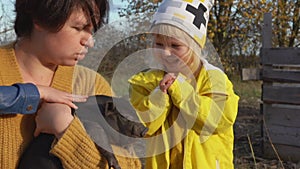 Little girl in a yellow raincoat is petting a black piglet held by a woman