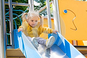 Little girl in a yellow sports sweater goes down the slide