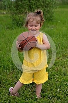 Little girl in yellow suit plays ball on lawn