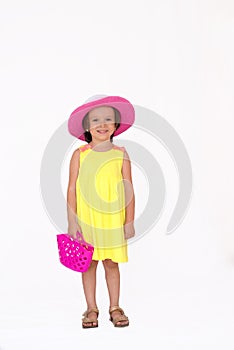 Little girl with yellow summer dress and pink hat holding a plastic toy bag, isolated