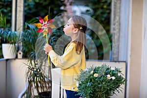 Little girl in a yellow sweatshirt on the balcony blowing on a windmill