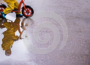 Little girl in yellow waterproof clothes with bike near a puddle