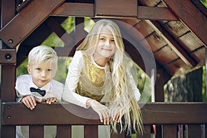 The little girl and younger brother look out the window of a small toy house.