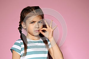 Little girl zipping her mouth on color background. Using sign language