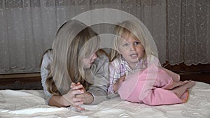 Little girls in the bedroom by the bed. The older girl teaches her little sister to count