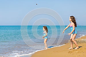 Little girls in bright swimsuits play on the beach. Children on vacation. Family vacation. happy sisters