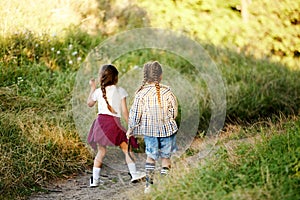 Little girls, children in casual clothes, holding hands, walking in meadow on warm sunny day. Girl scouts