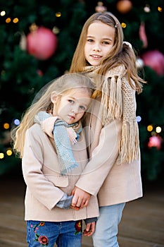 Little girls in coats near large Christmas tree