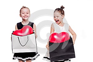 2 little girls with elegant dresses hold large bags with heart-shaped balloons inside