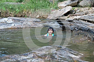 Little girls enjoy swimming in the river. Cute Asian girl wearing a life jacket is having fun playing in the stream. Healthy