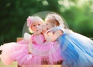 Little girls in evening dresses telling secrets on the bench. Copy space