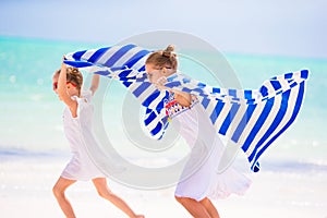 Little girls having fun running with towels on tropical beach with white sand and turquoise ocean water