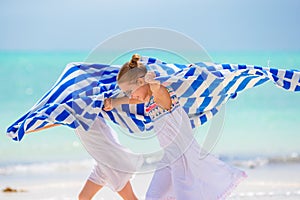Little girls having fun running with towels on tropical beach with white sand and turquoise ocean water