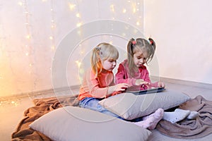 Little girls involved in use of tablet and sit on floor in brigh