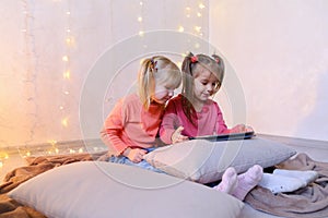 Little girls involved in use of tablet and sit on floor in brigh