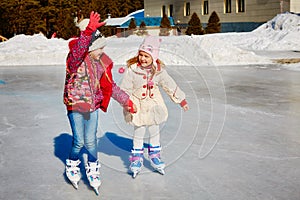 Little girls learn to skate. They are laughing and happy. Concept of friendship and fun holidays.