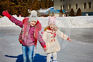 Little girls learn to skate. They are laughing and happy. Concept of friendship and fun holidays.