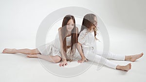 Little girls with long hair in white clothes play, indulge and tickle each other