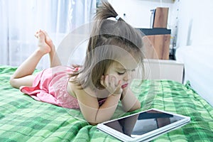 Little girls looking on pad lying on bed. Children time spending. Kids using tablet computer