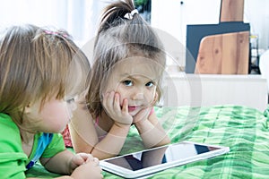 Little girls looking on pad lying on bed. Children time spending. Kids using tablet computer