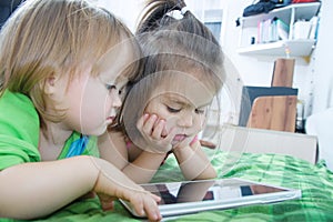 Little girls looking on pad lying on bed at home