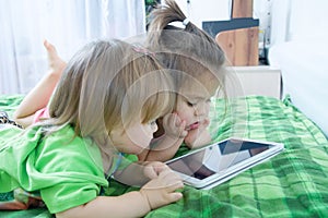 Little girls looking on pad lying on bed at home. Children time spending