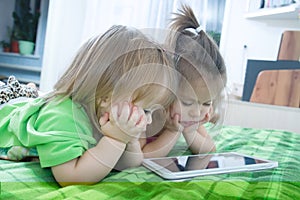 Little girls looking on pad lying on bed at home. Children time spending. Kids using tablet