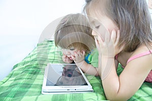 Little girls looking on pad lying on bed at home. Children time spending. Kids using tablet
