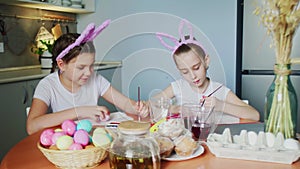 Little girls paints eggs. They draws Easter patterns on eggs.