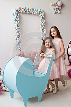 Little girls in pink dresses play with a blue stroller like little moms