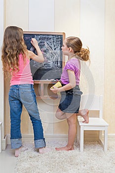 Little girls in the playroom paint on the blackboard