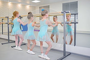 Little girls practicing ballet in studio near barre. Concentrating on exercise, view from back.