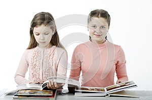 Little girls read books at the table on white