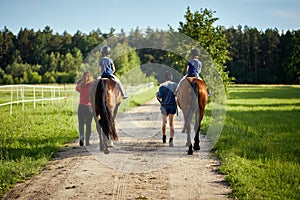 Little girls ride beautiful horses on the road in the forest in summer