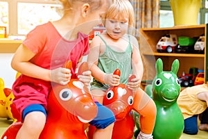 Little girls riding on play horses in kindergarten