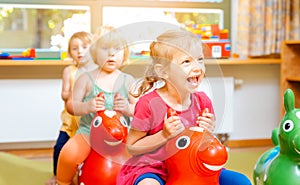 Little girls riding on play horses in kindergarten photo