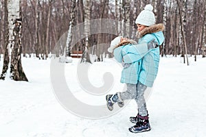 Little girls, sisters are walking, having fun in snowy winter park. Stylish clothes, blue jackets with fur,warm pants with