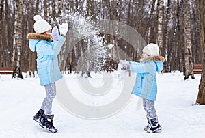 Little girls, sisters are walking, having fun in snowy winter park. Stylish clothes, blue jackets with fur,warm pants with