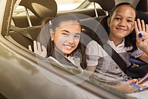 Little girls sitting on a backseat of a car looking camera going to school by car and waving goodbye. Transportation concept