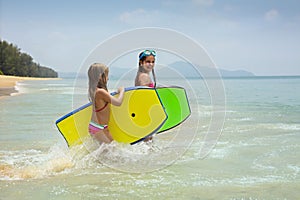 Little girls with surfing boards playing on tropical ocean beach. Summer water fun for surfer kids