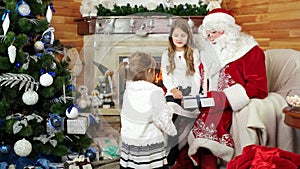 Little girls visit santa at his residence, happy sister sitting on santa claus lap, christmas gifts