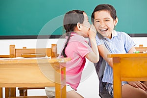 Little girls whispering and sharing a secret in classroom