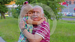 Little grandchild kid embracing kissing with her grandfather in park, happy family relationship