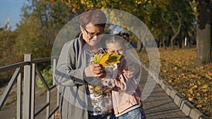 Little granddaughter with bunch of autumn yellow leaves, runs to his beloved grandmother in the Park and embraces her.